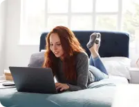 Young woman on a bed with a laptop searching for flatshare options online, reflecting modern home searching and student living.